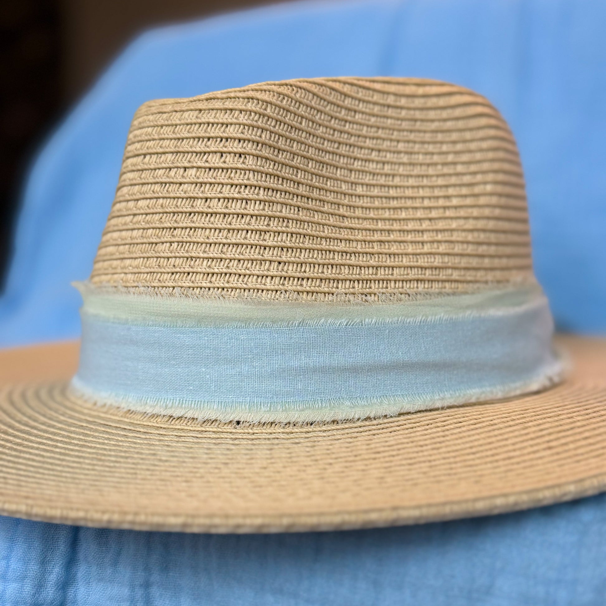 Beige straw hat with a light blue band on a blue fabric background