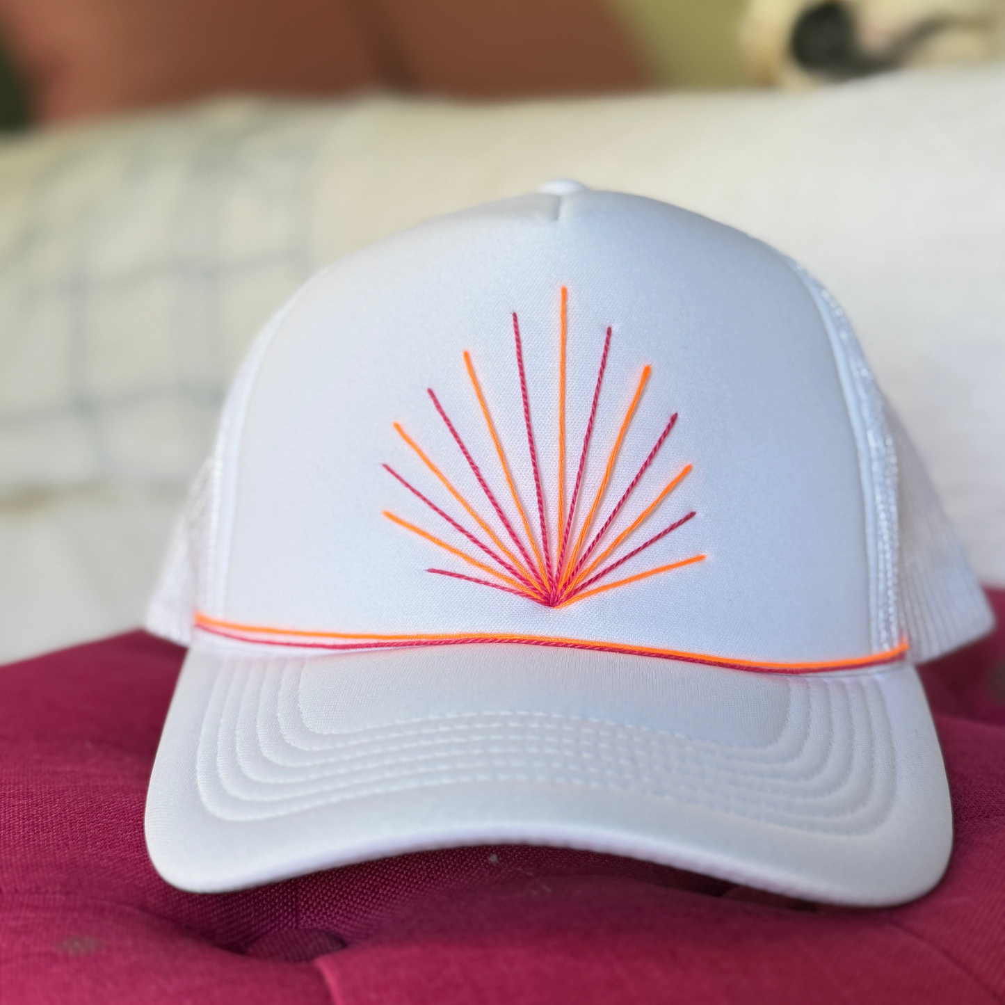 White cap with orange and red design on a pink surface