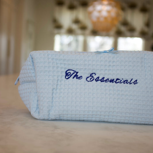 Light blue pouch with 'The Essentials' text on a blurred indoor background